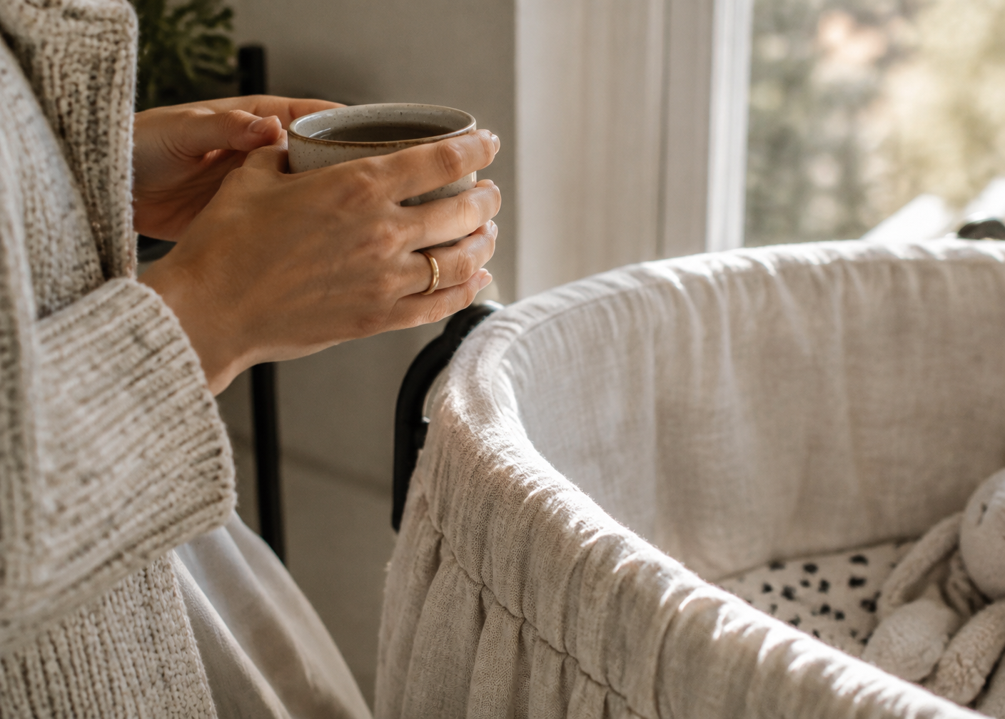 Mother holding a mug beside a linen bassinet